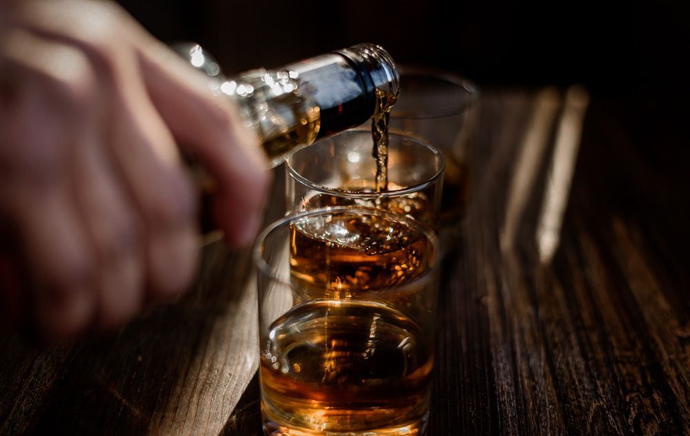 Pouring strong alcohol drink into the glasses which are on the wooden table