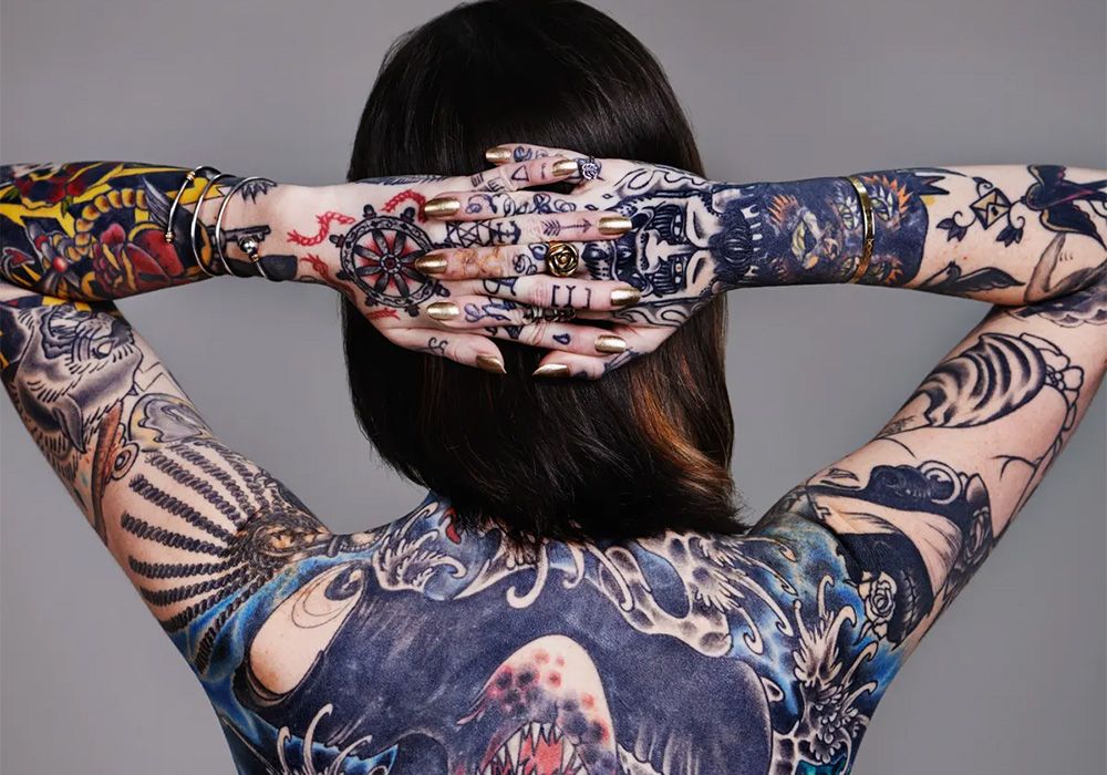 Tattooed woman standing backwards with hands clasped behind the head