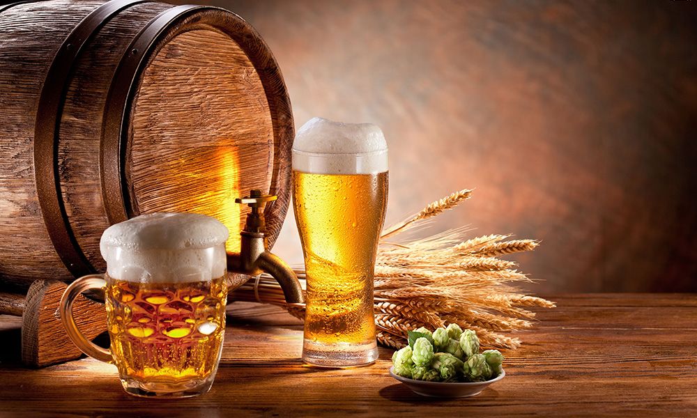 Two mugs with beer in the background barrel