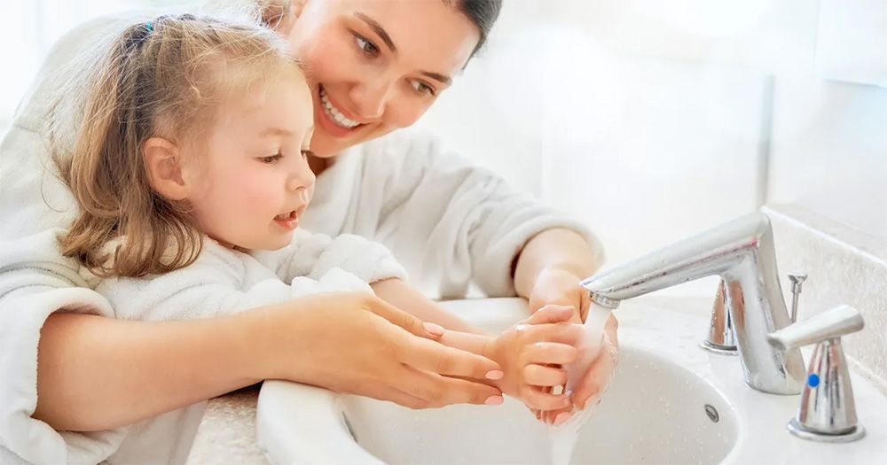 Woman helps little girl wash her hands